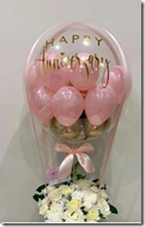 6 pink balloons stuffed in a clear balloon with a basket of 12 white flowers