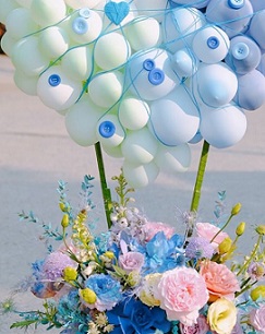 20 Blue Balloons cluster on top held with sticks on a basket of pink blue and yellow roses flowers
