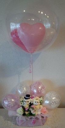 Clear Bobo balloon with pink and white balloons inside Tied to a basket with 4 pink and white balloons and 2 teddy bears and 6 pink and white roses