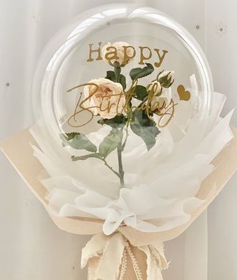 A bouquet of single clear balloon with happy birthday printed wrapped in white and jute with one white rose inside the balloon